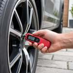 Red digital tyre pressure gauge being used on a car tyre valve